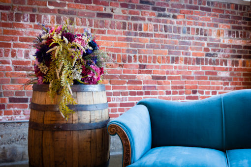 Vintage wine barrel used as a side table next to an antique blue velvet couch. Florals on the barrel. Styled lounge setting at a launch party.