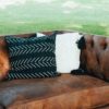 Side angle view of the corner of the Lewes leather couch. Seen here is half of the couch with tufted back and arm and 1 cushion. Two pillows (black and white) in the corner.