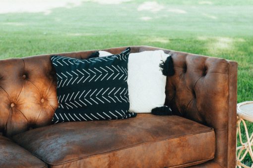 Side angle view of the corner of the Lewes leather couch. Seen here is half of the couch with tufted back and arm and 1 cushion. Two pillows (black and white) in the corner.