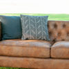 Showing two thirds of the Lewes brown leather couch. Tufted back, two smooth cushions and two black pillows in the corner.