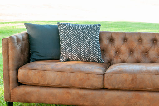 Showing two thirds of the Lewes brown leather couch. Tufted back, two smooth cushions and two black pillows in the corner.