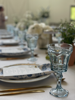 Mismatched blue goblets in focus with florals and long table in background at wedding reception