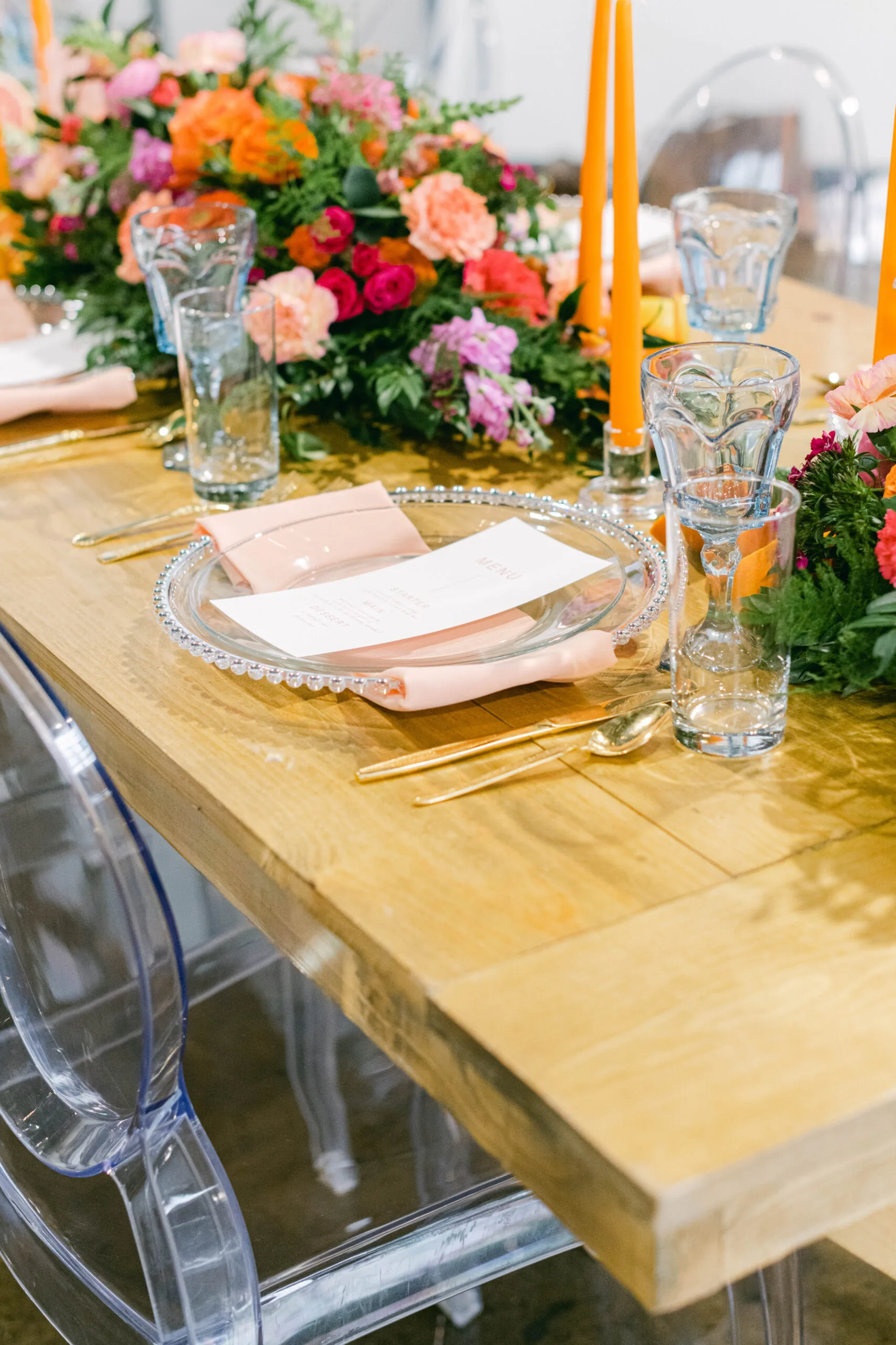 Water goblets at dinner party WEBP Tablescape with clear dinner plates, light blue goblets, orange candles with clear glass candlesticks.