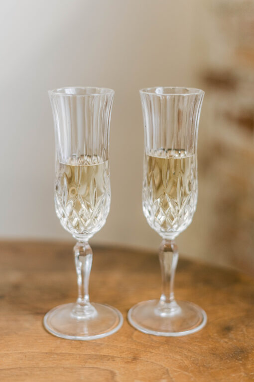 Two ornate champagne flutes with wine, sitting on a dark wood table