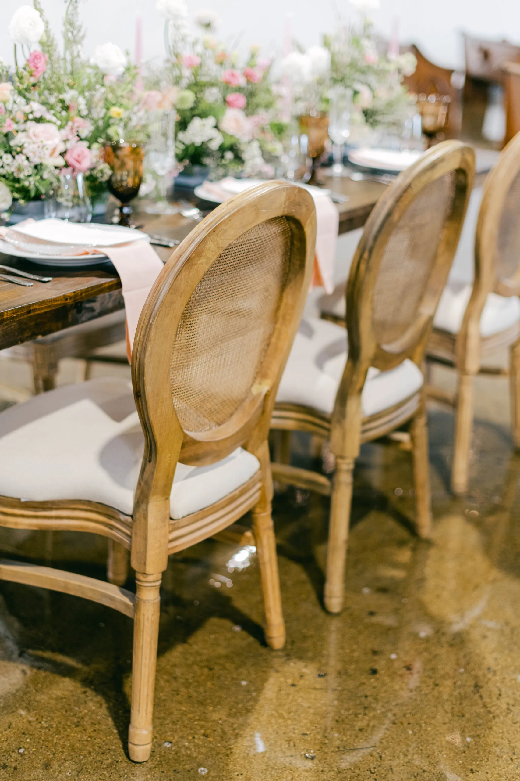 French cane back chairs at reception WEBP Cane backed wooden chairs at a wedding reception with dark wood farmtables.