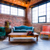 Launch event with a lounge seating area featuring a velvet blue vintage sofa, a green armchair to the left, a pink armchair to the right, a large wooden coffee table in front of the sofa and sitting on a large area rug.