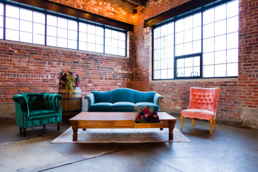 Launch event with a lounge seating area featuring a velvet blue vintage sofa, a green armchair to the left, a pink armchair to the right, a large wooden coffee table in front of the sofa and sitting on a large area rug.