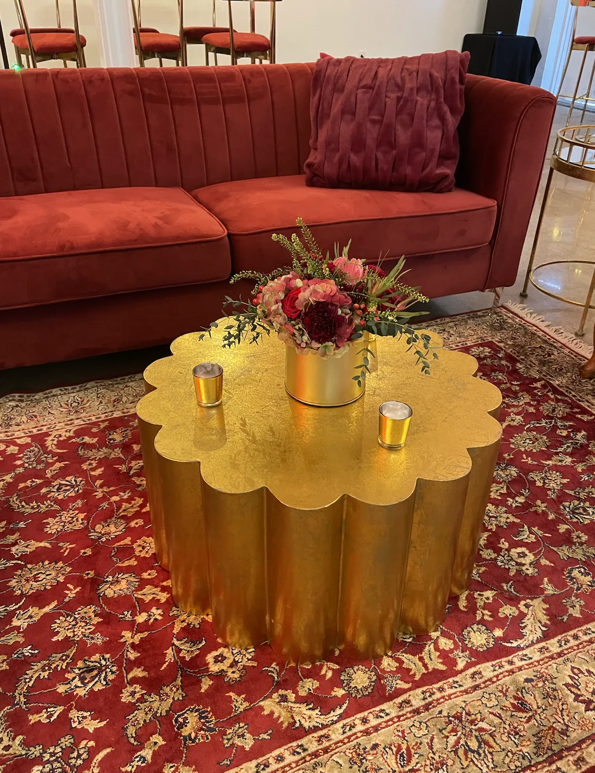 Lounge with red sofa and gold coffee WEBP Red velvet couch on a rug patterned rug with a bright gold scalloped coffee table.