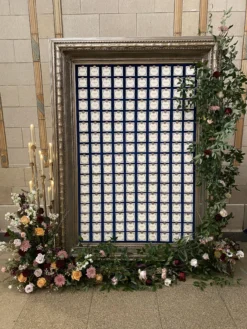 Oversized frame with florals on edges. In the center are seating cards for wedding reception