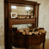 Side view of half moon desk pushed up against a tall wooden mantle with mirror. Used to display desserts at wedding