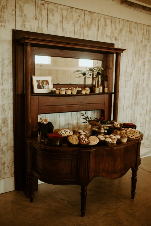 Side view of half moon desk pushed up against a tall wooden mantle with mirror. Used to display desserts at wedding