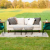 White Ella Sofa sitting outside in a field. Two green velvet chairs, two ottomans, and a rug sitting on the grass for a photo shoot.