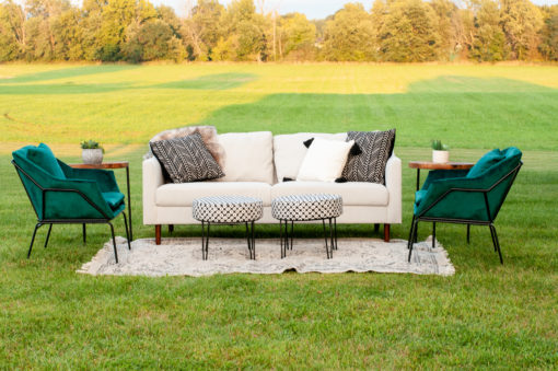 White Ella Sofa sitting outside in a field. Two green velvet chairs, two ottomans, and a rug sitting on the grass for a photo shoot.