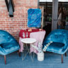 Two blue velvet armchairs with a side table in between and a larger table with pink tablecloth.