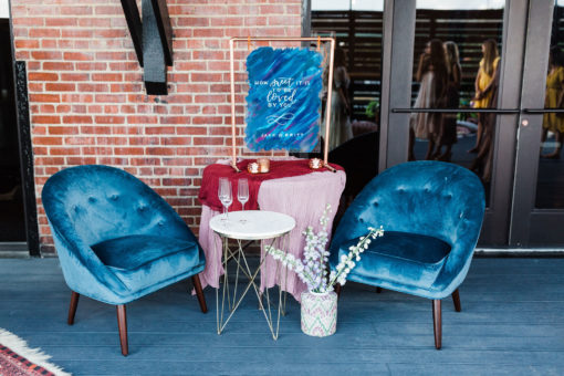 Two blue velvet armchairs with a side table in between and a larger table with pink tablecloth.