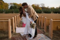 Couple kissing in an outdoor wedding with church pews and rugs for the aisle