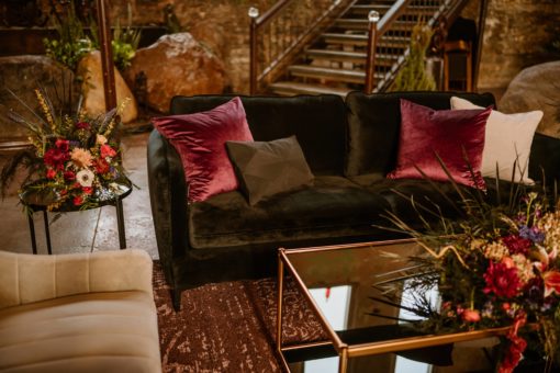 Black sofa with gray barrel armchair and black glass coffee table. Decorated with flowers. Boho lounge area at an event.