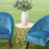 Two blue velvet chairs of mid-century modern style. Round rattan side table in between with a plant in a white vase on the table.