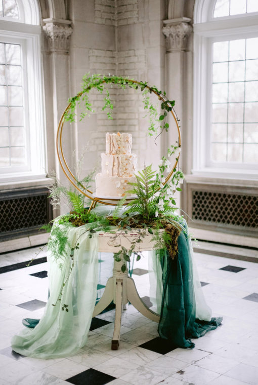 Three tiered wedding cake sitting on ornate vintage round table with a big circle decor and greenery