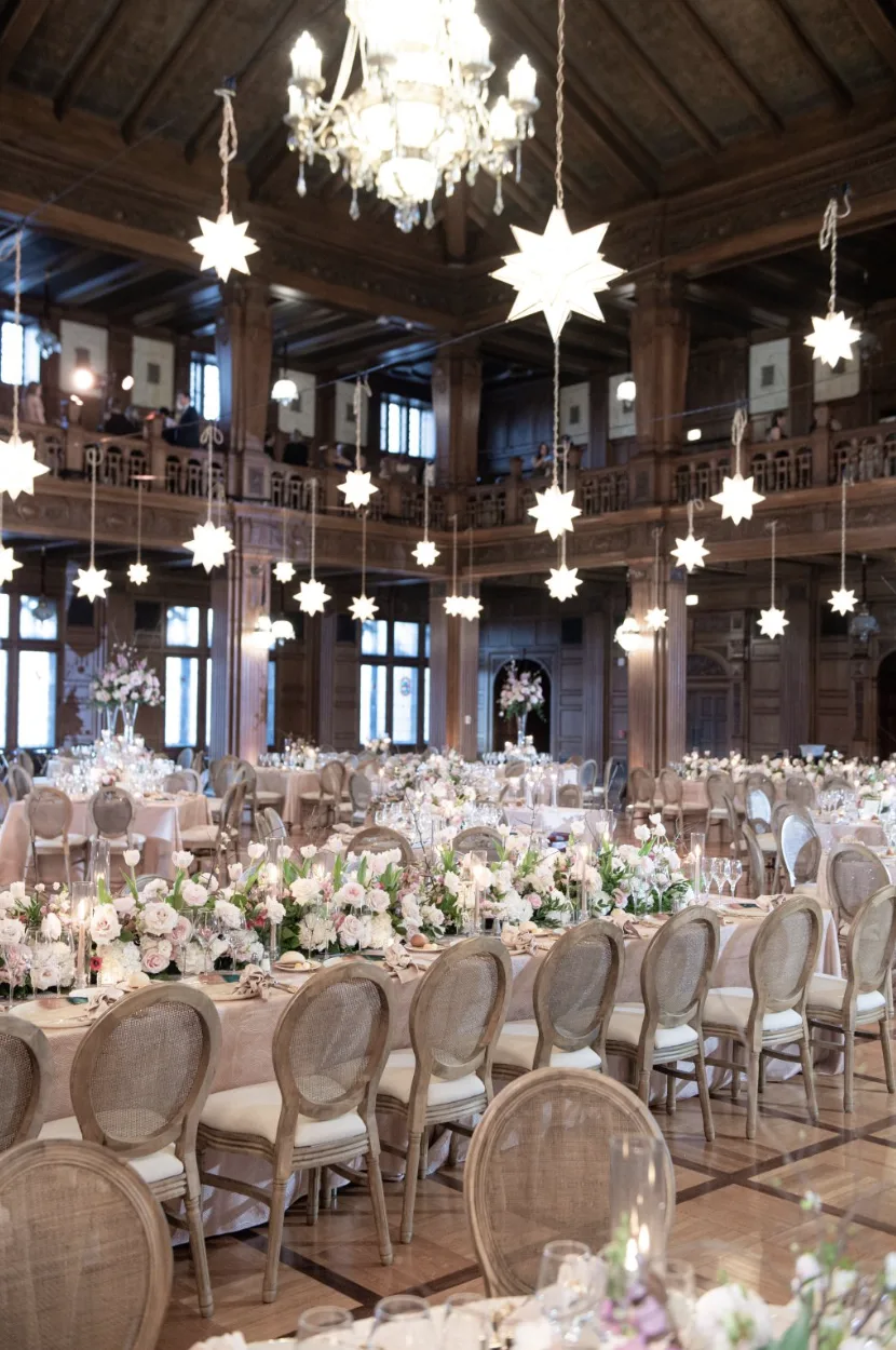 Louis Chairs at Scottish Rite WEBP A grand hall filled with round-back wooden chairs with upholstered seats, arranged at elegantly decorated wedding reception tables with floral centerpieces and candles