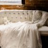 Cream loveseat with tufted button back and wooden arms and legs. Wedding dress laying on loveseat. Against a brick wall.