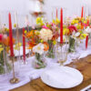 Bold color tablescape wtih brass candlesticks, yellow goblets, red candles and white plates.