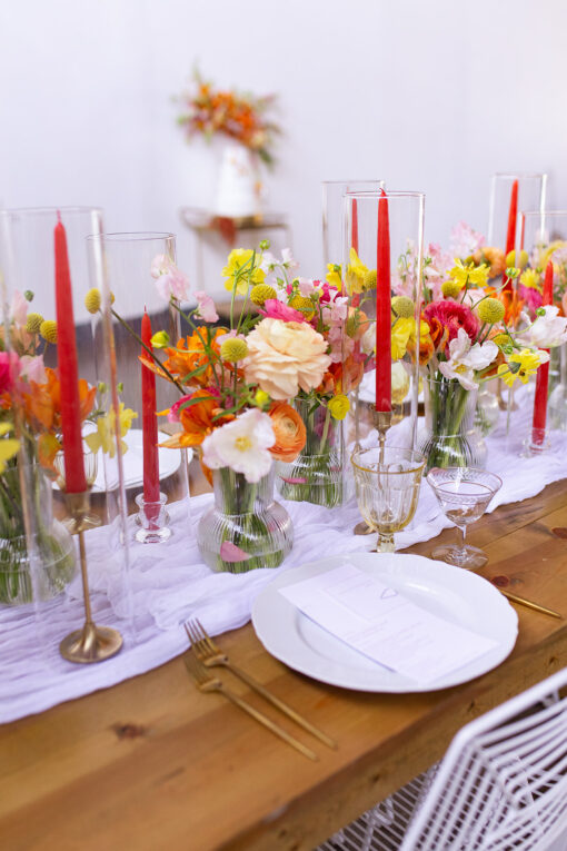 Bold color tablescape wtih brass candlesticks, yellow goblets, red candles and white plates.