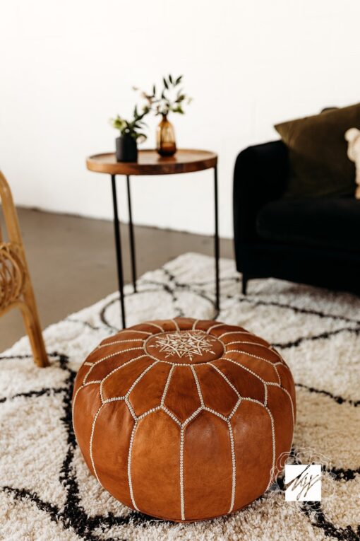 Brown leather pouf sitting on a black and white shaggy rug with black sofa and side table in the background