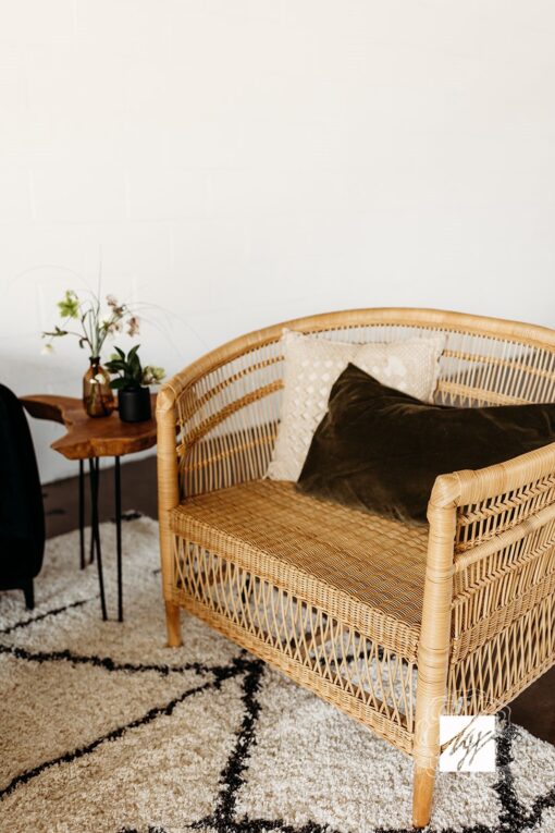 Overside wicker rattan chair with pillows sitting on a black and white rug. White walls in background.