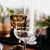 Clear coupe with a wide rim on a table with brown goblet and white candle behind.