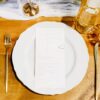 White dinner plate with menu against a warm wood table with gold flatware and orange hues.