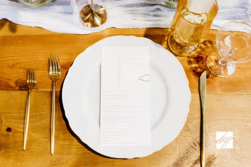 White dinner plate with menu against a warm wood table with gold flatware and orange hues.