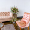 Lounge seating area with blush velvet sofa, pink armless accent chairs and a rug. Florals on a table.