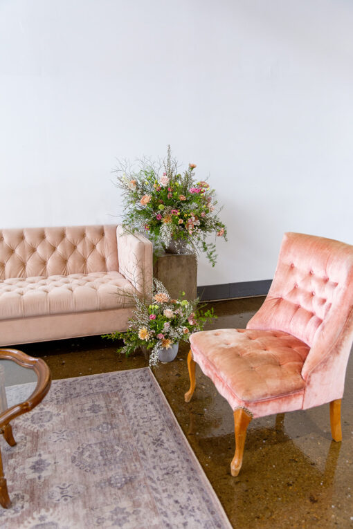 Lounge seating area with blush velvet sofa, pink armless accent chairs and a rug. Florals on a table.