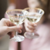 Close up on two vintage coupes with gold rims being held by 2 people in a toast.