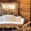 Vintage white sofa with tufted back in three panels with one solid cushion. Grass wall in background with neon light with the couple's last name. Wood panel in background at wedding reception photo booth