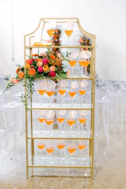 Gold framed bookshelf with orange liquid in wine glasses as a welcome drink to a wedding reception