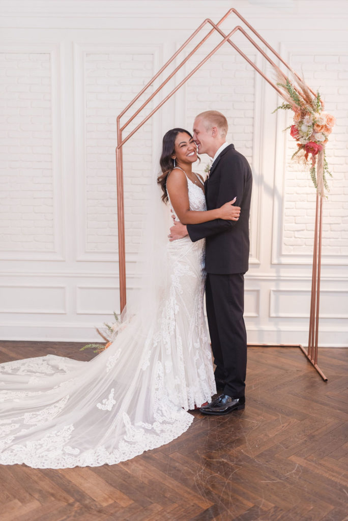 A young diverse couple standing in from of the Colleen Copper arch for a wedding ceremony.