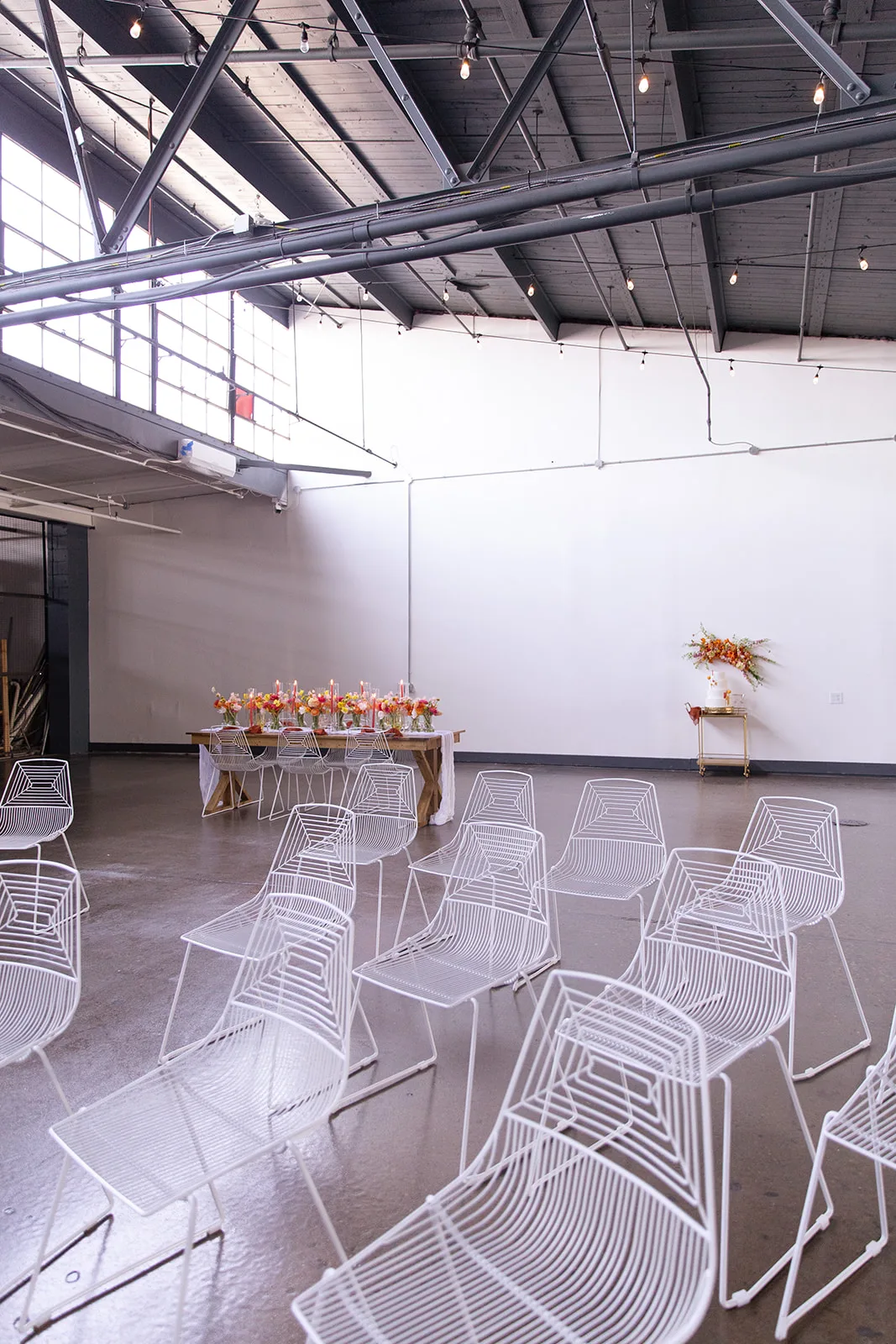 White wire chairs in industrial venue in Indy WEBP White wire chairs set up in a semi-arch on a concrete floor