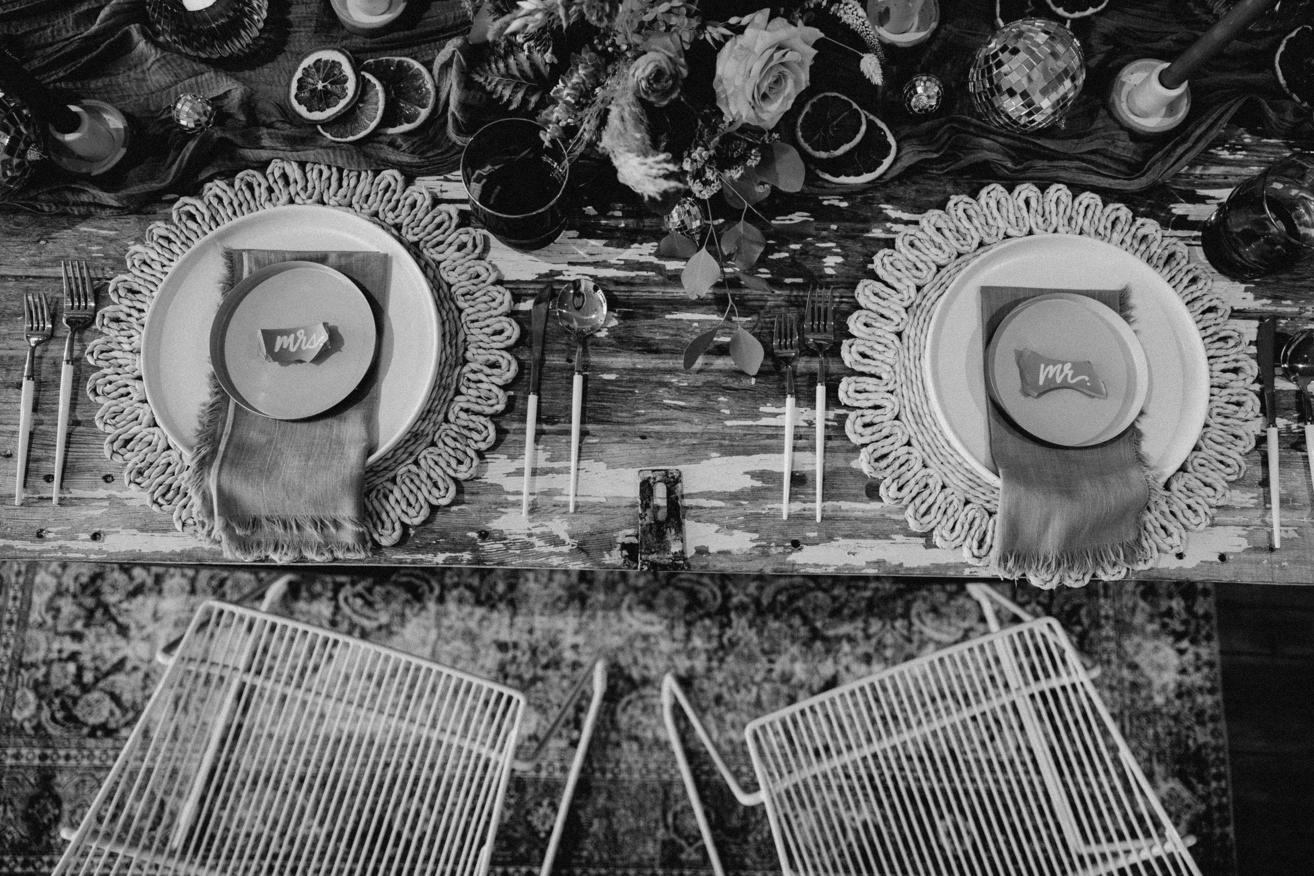 black and white photo with the white wire metal chairs WEBP Black and white arial photo of a sweetheart table at a wedding reception. Boho tablescape and white wire modern chairs