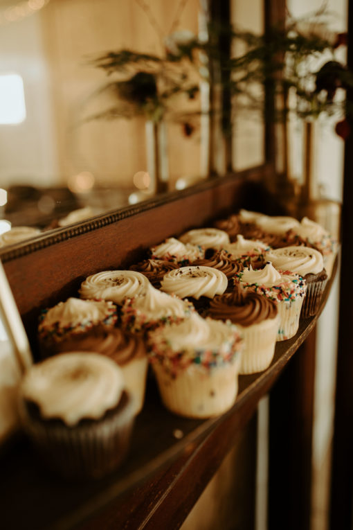 Close up on cupcakes on the shelf of a dark wood vintage mantle with a mirror