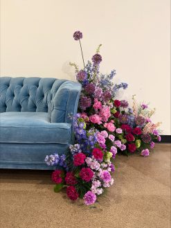 Quarter of blue velvet sofa with pink and purple florals on the floor and crawling up the side