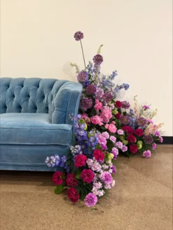 Quarter of blue velvet sofa with pink and purple florals on the floor and crawling up the side