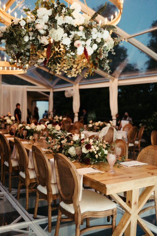 Solid wood farm tables with matching Louis chairs under a clear tent at wedding reception in Noblesville, Indiana