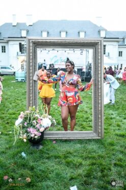 Giant free standing frame with a black woman posing in the center. On grass outside of the Lilly house at Newfields
