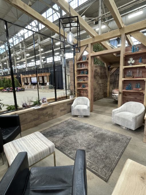 Expo event seating area with two swivel gray barrel chairs, gray rug, and black arm chairs under a wooden room structure