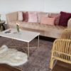 Light pink modern sofa with pillows, furry white accent chair and rattan accent chair around a white modern coffee table on a rug.