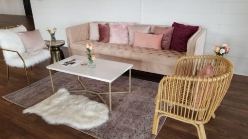 Light pink modern sofa with pillows, furry white accent chair and rattan accent chair around a white modern coffee table on a rug.