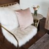 Metal gold chair with two giant fuzzy white cushions on the seat and back. Light pink square pillow