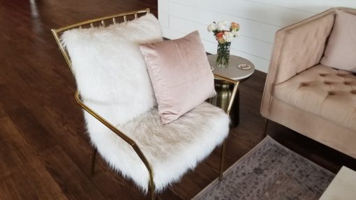 Metal gold chair with two giant fuzzy white cushions on the seat and back. Light pink square pillow